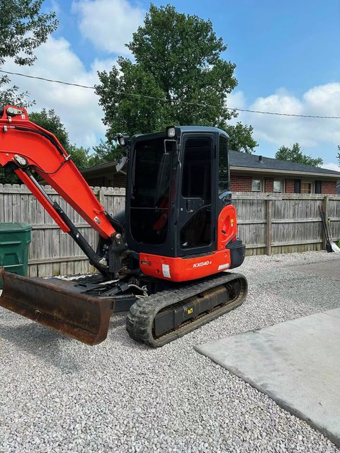 Compact excavator with tinted cab glass parked on a gravel drive